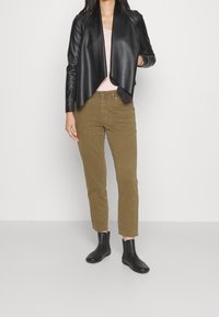 Veste en cuir noire avec un devant asymétrique, haut rose pâle en dessous, pantalon vert olive et bottines noires.