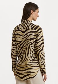 Langermet skjorte med et beige og brunt tigermønster. Har krage og knapplukking ved mansjettene, med en avslappet passform og buet kant.