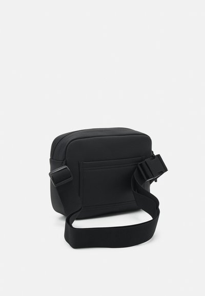 Sac en bandoulière rectangulaire noir avec une surface texturée, fermeture à glissière, sangle réglable et poche avant. Design compact et léger.