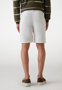 White linen shorts, tailored fit, with side pockets and a rolled hem. Paired with brown suede shoes for a casual look.