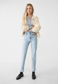 Helles graues Henley-Shirt mit einer cremefarbenen, oversized Strickjacke. Tragen Sie es mit hochgeschnittenen hellblauen Jeans und schwarzen Loafers. Einfaches, klares Design.