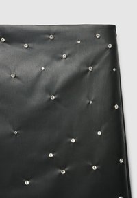 Schwarzes Kunstleder mit glatter Textur, das mit einem verstreuten Muster aus diamantähnlichen Nieten gestaltet ist.