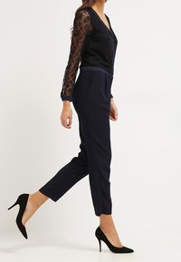 Černý krajkový top s dlouhými rukávy v kombinaci s námořnicky modrými zúženými kalhotami s pasovým páskem a úzkým střihem. Nosit se černými vysokými podpatky.