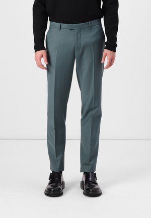 Trousers in a muted teal color, made of smooth fabric, featuring front pleats and a tailored fit, paired with black shoes.