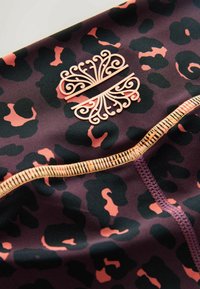 Leopardų rašto audinys tamsiai purpurinės ir juodos spalvos, su persikų akcentais. Prieduose yra dekoratyvi emblema ir kontrastingos siūlės detalės.