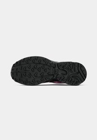 Black outsole of a shoe featuring a textured tread pattern with triangular lugs, contrasting pink accents near the heel.
