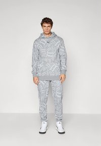 Conjunto de sudadera con capucha y pantalones deportivos grises con patrones geométricos, hecho de tela suave con puños acanalados y un bolsillo tipo canguro. Zapatillas deportivas blancas.