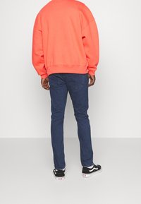 Felpa oversize corallo, jeans blu, sneakers nere con dettagli bianchi. Cuciture visibili sui jeans e polsini a coste sulla felpa.