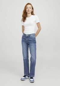 Balta trumpomis rankovėmis marškiniai, mėlyni džinsai tiesaus kirpimo, mėlynos ir baltos sportinės bateliai. Paprastas dizainas, kasdieniškas siluetas, minimalus detalizavimas.