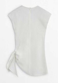 Haut blanc sans manches à col montant, avec un détail noué sur le côté et une texture lisse, conçu avec un ourlet arrondi et une lueur subtile.