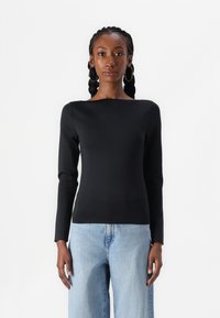 Black long-sleeve top with a boat neckline, smooth texture, slim fit, paired with light blue wide-leg jeans. Simple, modern design.