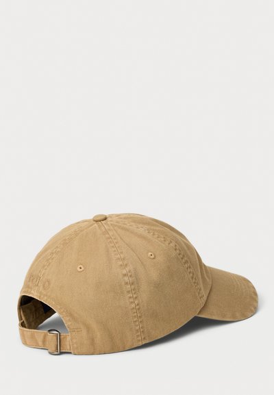 Khaki cotton baseball cap with a curved brim, rear adjustable strap, and embroidered logo on the side. Textured fabric, six-panel design.