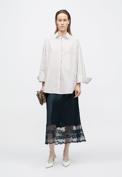 Pruhovaná košeľa na gombíky v bielej a červenej farbe; doplnená o čiernu saténovú sukňu s čipkovaným lemom. Doplnky zahŕňajú leopardím vzorovanú kabelku a biele lodičky.