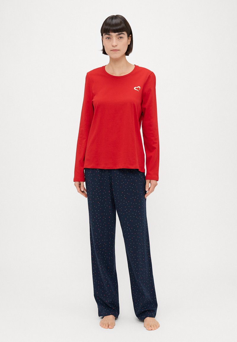 Rotes langärmliges Oberteil mit einem kleinen weißen Herzlogo und marineblauen Druckhosen mit kleinen roten und weißen Punkten. Weiches, atmungsaktives Material.