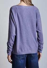 Ljuslila långärmad topp med avslappnad passform, mjuk textur och samlad detalj vid ärmarna, i kombination med mörkblå jeans.