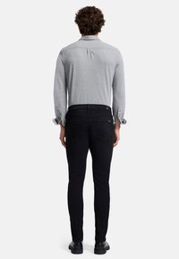 Grå langærmet skjorte med knapmanchetter, parret med sorte slim-fit jeans. Glat stof, enkelt design, og baglomme detaljer synlige.