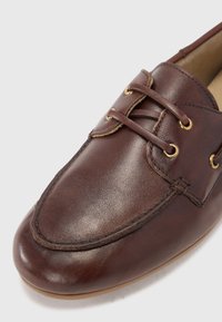 Scarpa da barca in pelle marrone con punta arrotondata, cuciture a contrasto e eyelets in tonalità oro per i lacci. Texture liscia con finitura lucida.