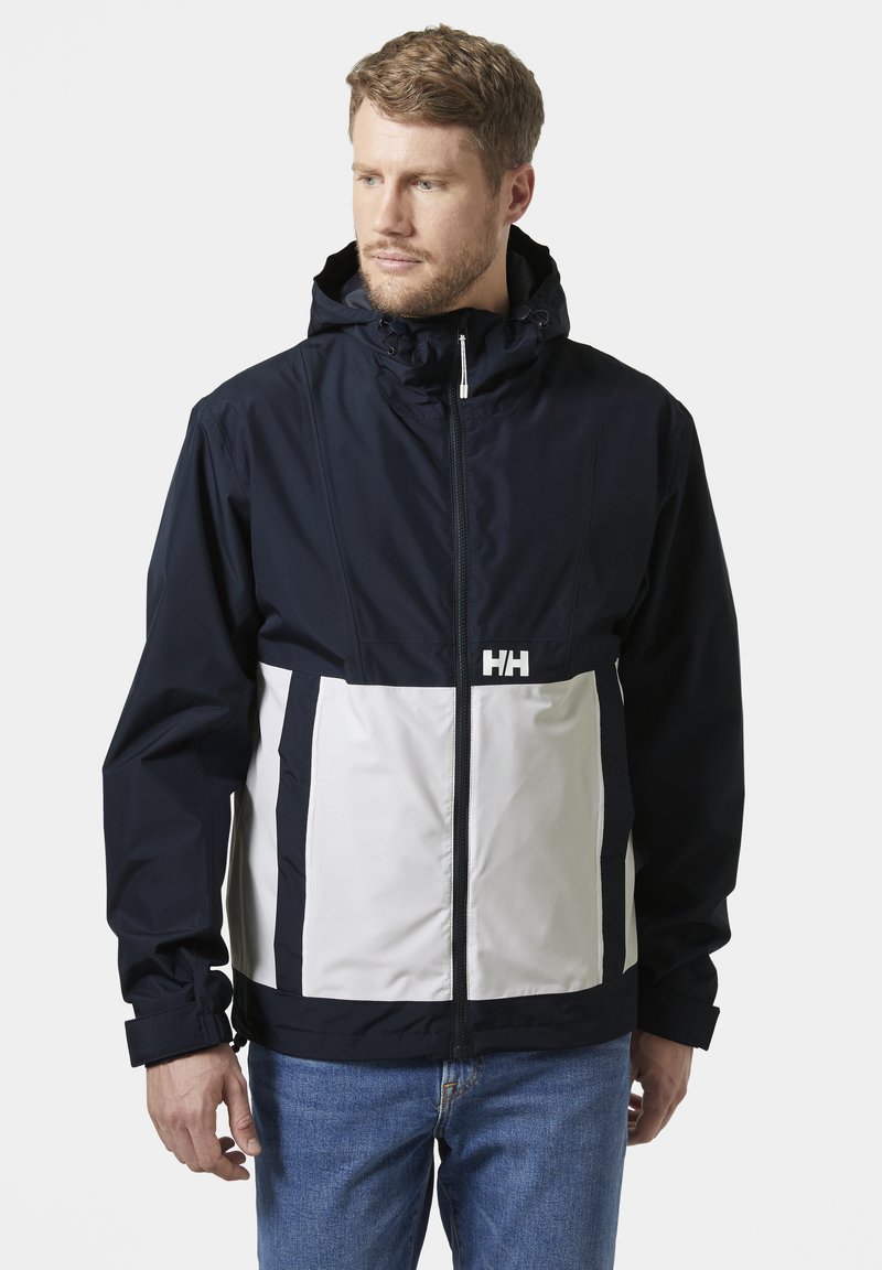 Marineblauwe en lichtgrijze waterdichte jas met een ritssluiting, verstelbare capuchon en prominent HH-logo op de borst. Casual ontwerp.