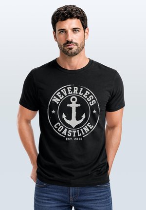Mann mit kurzen lockigen Haaren, der ein schwarzes T-Shirt mit einem weißen Anker und dem Text "Nevertheless Coastline Est. 2016" trägt, steht vor einem schlichten Hintergrund.