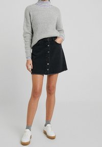 Svart denimkjol med knappstängning fram och fransad nederkant. Kombinerad med en ljusgrå ribbad tröja och vita sneakers.