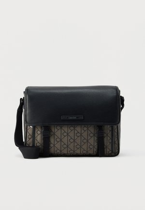 Schwarz-braune Calvin Klein Umhängetasche mit verstellbarem Riemen, Klappenverschluss und wiederholtem "CK"-Logo-Muster auf dem Stoffkörper.