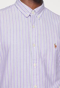 Chemise boutonnière mauve clair avec des rayures blanches et bleues, dotée d'un col classique et d'un petit logo brodé sur la poitrine.