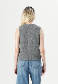 Top grigio senza maniche realizzato in maglia con una consistenza morbida, scollatura tonda e un design aderente, abbinato a jeans a vita alta di un blu chiaro.