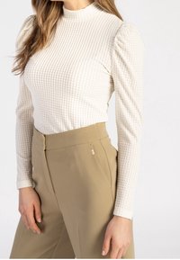 Vit strukturerad långärmad topp med hög krage, kombinerad med beige högmidjade byxor med en snygg design och sidfickor.