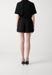 T-shirt noir à manches courtes associé à un short noir. Le matériau semble léger et texturé. Porté avec des sandales à talons noirs.