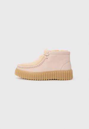 Bottes de cheville en daim rose clair avec doublure en fausse fourrure beige et semelle en caoutchouc épaisse et rainurée. Présente un minimum de coutures et un design à lacets.