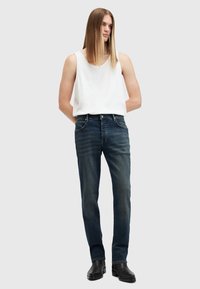 Top blanco sin mangas combinado con jeans azul oscuro, con un diseño de pierna recta y un ligero desgaste, llevado con botas negras hasta el tobillo.