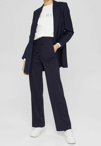 Blazer azul marino, sudadera blanca con letras de arcoíris, pantalones de tiro alto azul marino y zapatillas blancas. Tejido suave, corte recto, diseño minimalista.