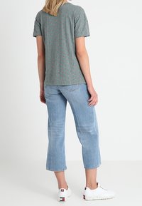 Grå T-shirt med et subtilt grønt mønster, korte ærmer, parret med lysblå cropped jeans og hvide sneakers med logo akcent.