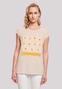 Beige short-sleeve t-shirt featuring a bold daisy pattern and yellow lettering reading "F4NT4STIC SUMMER" on the front. Soft fabric, relaxed fit.