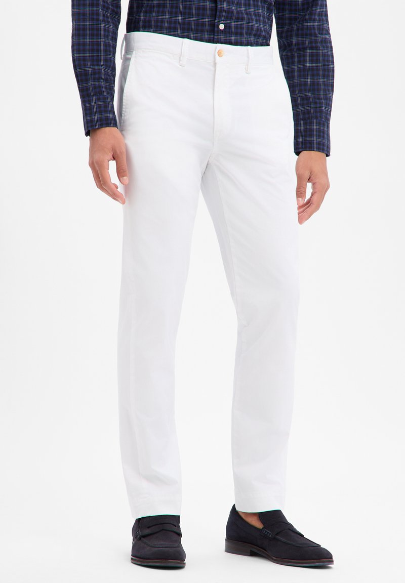 Weiße Baumwollhose mit glatter Textur, geradem Schnitt und Knopfverschluss am Bund, kombiniert mit dunklen Loafers.