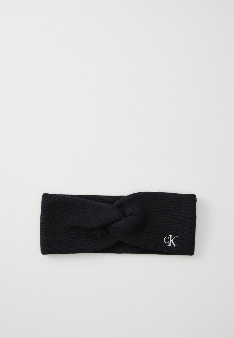 Donkerblauwe gebreide haarband met een gedraaide voorkant en geborduurde "ck"-logo in het wit aan de zijkant. Zachte textuur, brede vorm.