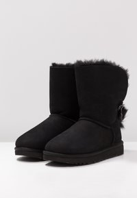 Bottines en daim noir à bout arrondi, doublure en fourrure douce sur le dessus et détail de fermeture éclair décoratif sur le côté. Semelle plate en caoutchouc.