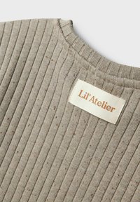 Žebrovaná béžová tkanina so subtílnymi hnedými fliačkami, s okrúhlym výstrihom a všitou etiketou, ktorá znie "Lil'Atelier."