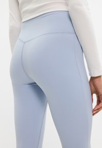 Leggings a vita alta di un blu chiaro realizzati in materiale elastico; texture liscia e design aderente con dettagli di cucitura sottili.