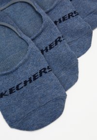 Zilas, zema nogriezuma zeķes, izgatavotas no teksturēta auduma ar ribotu augšdaļu, kuras izceļ logo "SKECHERS" tumši zilā krāsā visā virsmā.