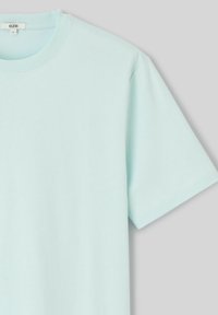 T-shirt bleu clair à col rond, manches courtes, taille large, suspendu sur un fond gris clair uni.