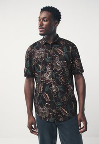 Chemise à manches courtes en tissu foncé avec des motifs floraux colorés. Dotée d'une fermeture à boutons et d'une coupe décontractée.
