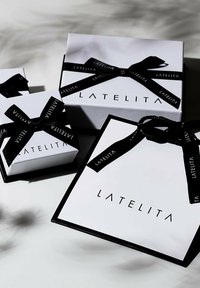 Three white gift boxes with black ribbon, featuring the word "LATELITA" printed in black. Boxes vary in size, with sleek designs and sharp edges.