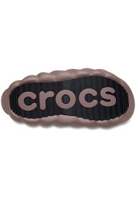 Bruine rubberen Crocs-zool met getextureerde zwarte zool en verhoogd "crocs" logo in een gladde, lichtbruine afwerking. Afgeronde, gewatteerde randen.