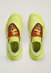 Felgele sportschoenen met oranje veters en zwarte rand, gezien van boven op een lichte achtergrond.