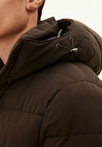 Bruine gewatteerde jas met een hoge kraag en verstelbare capuchon. Kenmerkt zich door een gequiltde textuur en een soepele ritssluiting met zwarte hardware accenten.