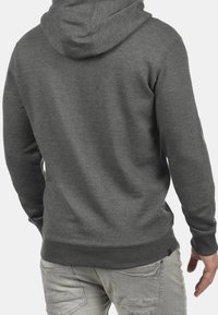 Man wearing a dark gray hooded sweatshirt and light gray jeans, shown from the back against a plain background.
