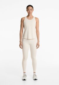 Beige atletisk linne och leggings gjorda av stretchigt material. Tätt sittande design med en slät yta och minimala sömmar. Vita sneakers.