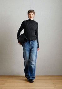 Čierny rebrovaný rolák, modré široké džínsy, čierna kožená kabelka a čierne topánky. Neutrálny pozadie s drevenou podlahou.