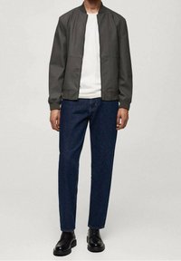 Chaqueta bomber gris oscuro, camiseta blanca y pantalones vaqueros azules. Zapatos negros con cordones. Textura lisa, diseño sencillo, puños elásticos en la chaqueta.